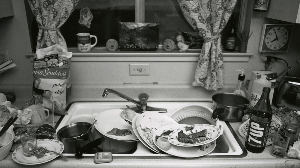 Black-and-white image of a sink overflowing with dirty dishes