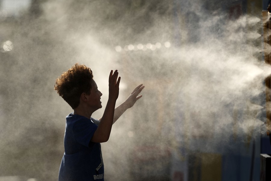 A person raises their arms, enjoying the coolness of water being sprayed from a mister.