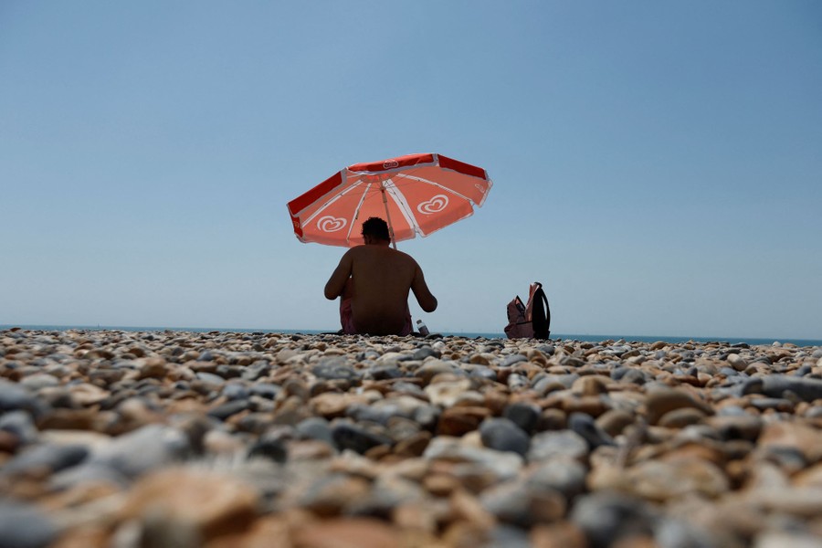 A man sits under an umbrella on a rocky beach.