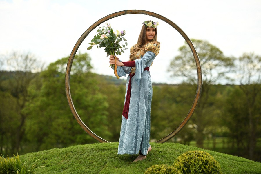 A model stands near a large circular sculpture, holding a bouquet