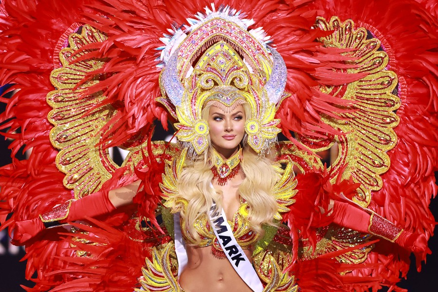 A woman participates in a beauty contest, wearing a huge, colorful, and feathery costume.