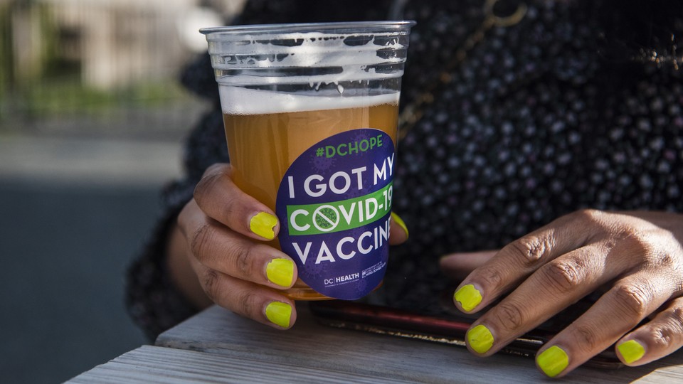 A picture of someone holding a glass of beer. The glass has a stick that reads "I got my COVID-19 vaccine."