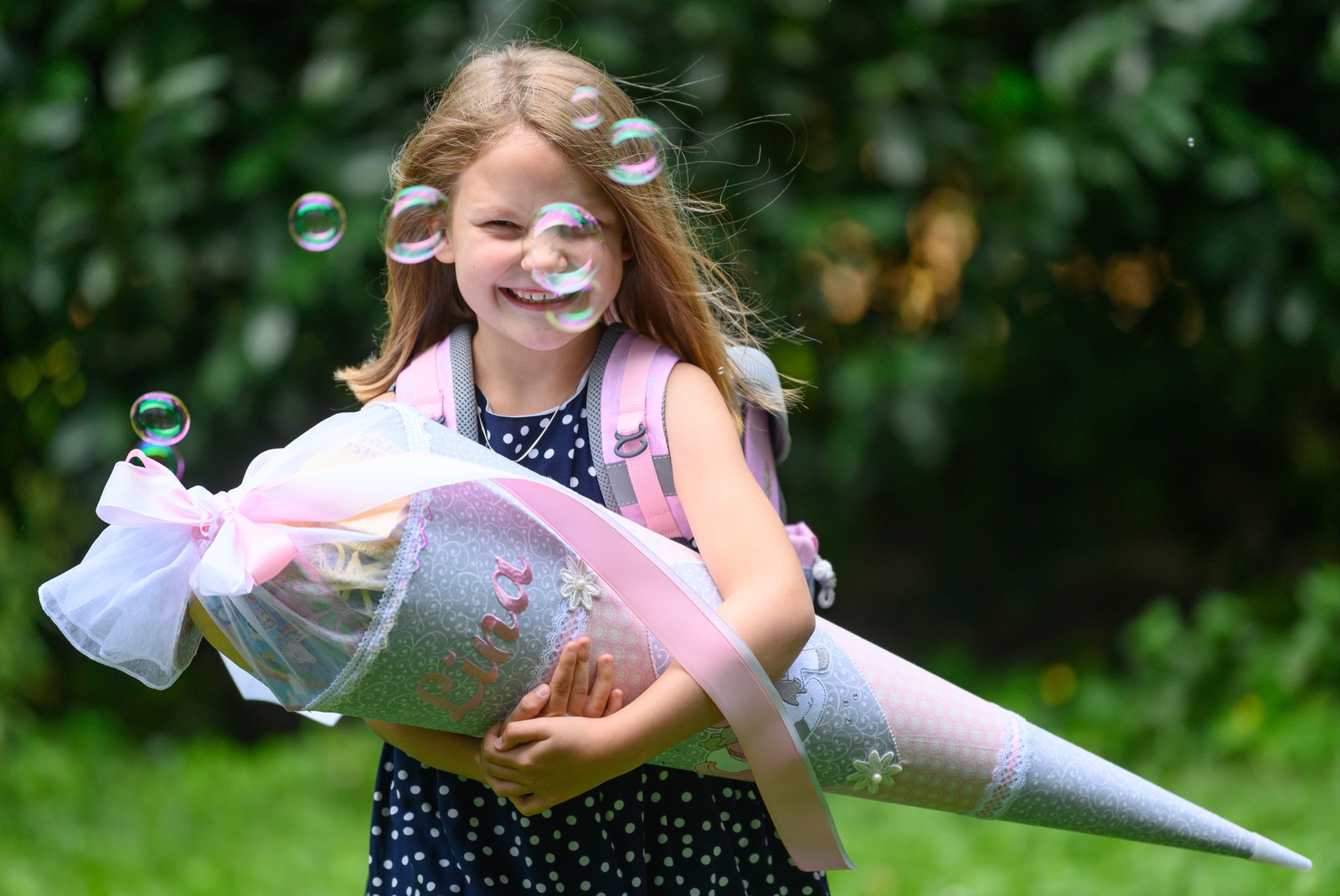 A smiling young girl holds a large decorated cone that is filled with treats and school supplies.
