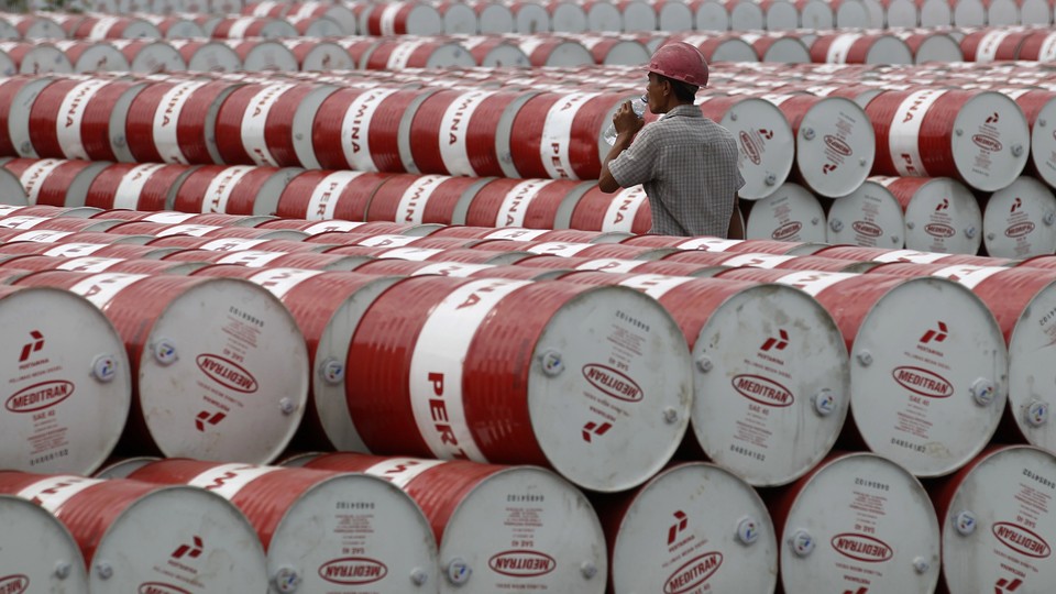 A worker walks between stacks of red and white oil barrels.