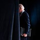A photograph of Joe Biden walking behind a curtain