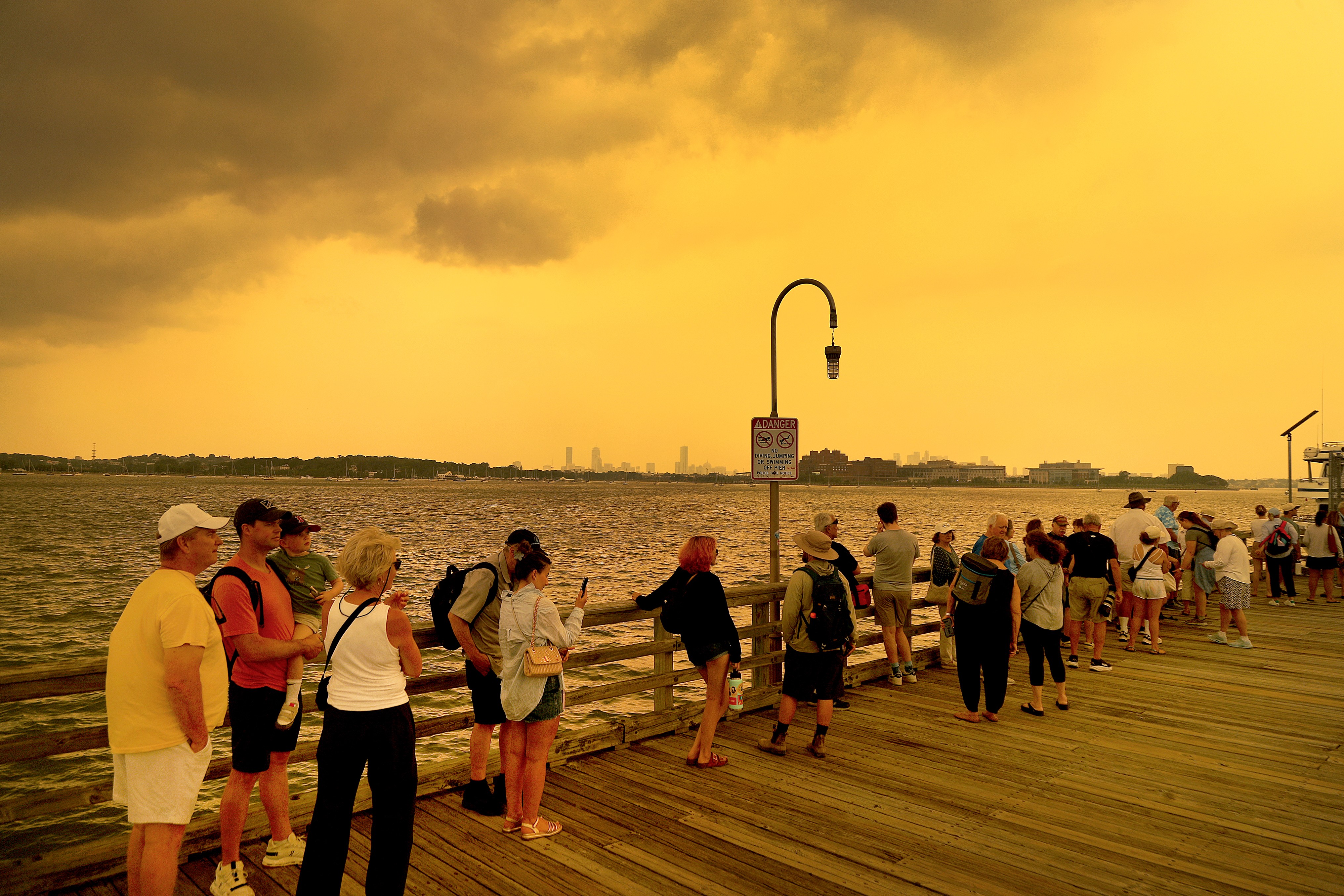 People look at a yellow sky from a ferry dock.