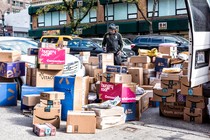 A deliveryman stands in a sea of subscription-service boxes on a sidewalk in NYC.