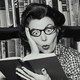A black-and-white photo of a shocked woman reading a book