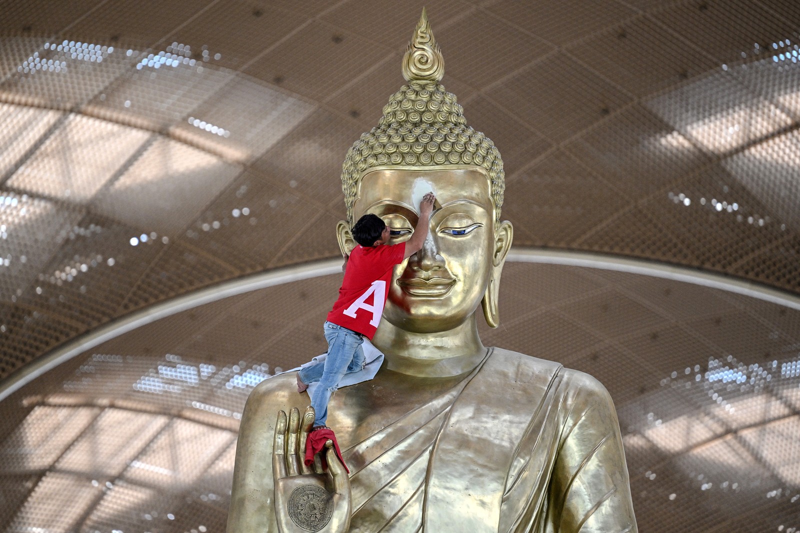 A worker cleans the face of a large statue of Buddha inside an airport.