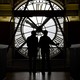 Two people are backlit while looking at a large clock
