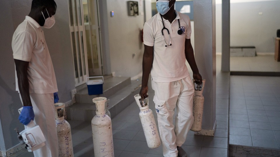 Two people who work for an emergency mobile service in Dakar, Senegal, carry oxygen tanks in a hallway