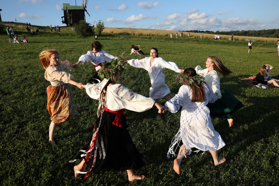 Six people in traditional clothing dance in a circle in a grassy field.
