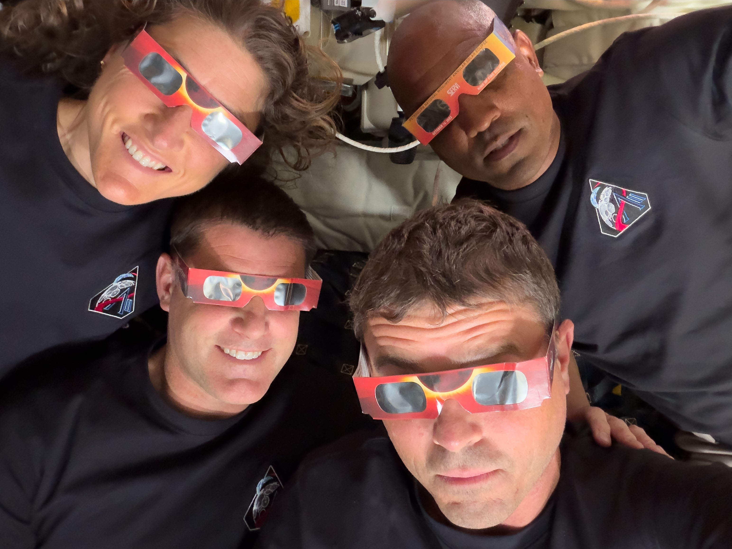 The four-person crew of Artemis pose for a photo, all wearing eclipse glasses.