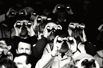 A black-and-white photograph of several men holding binoculars up to their faces to look at something far away