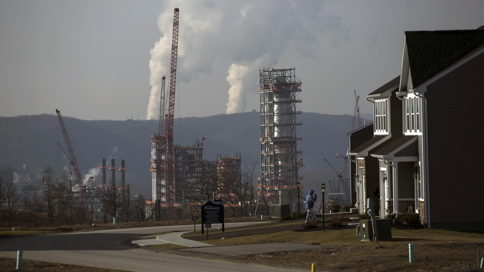 A smoking fracking project sits behind a suburban subdivision and beneath a gray, smoggy sky.