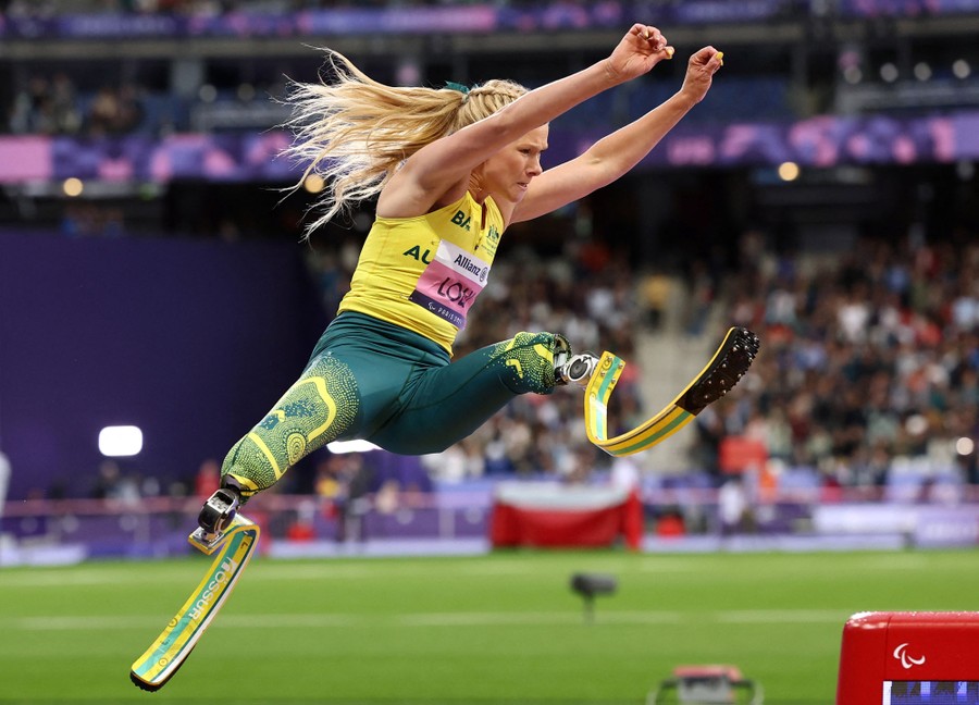 A para-athlete with prosthetic legs leaps during a long-jump event.