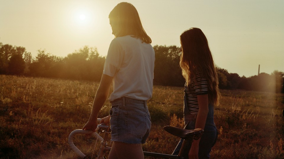 Two friends walking with a bike in a field