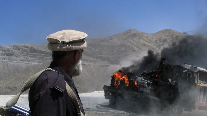 A Pakistani security official stands near a burning vehicle after it was attacked in the Balochistan region.