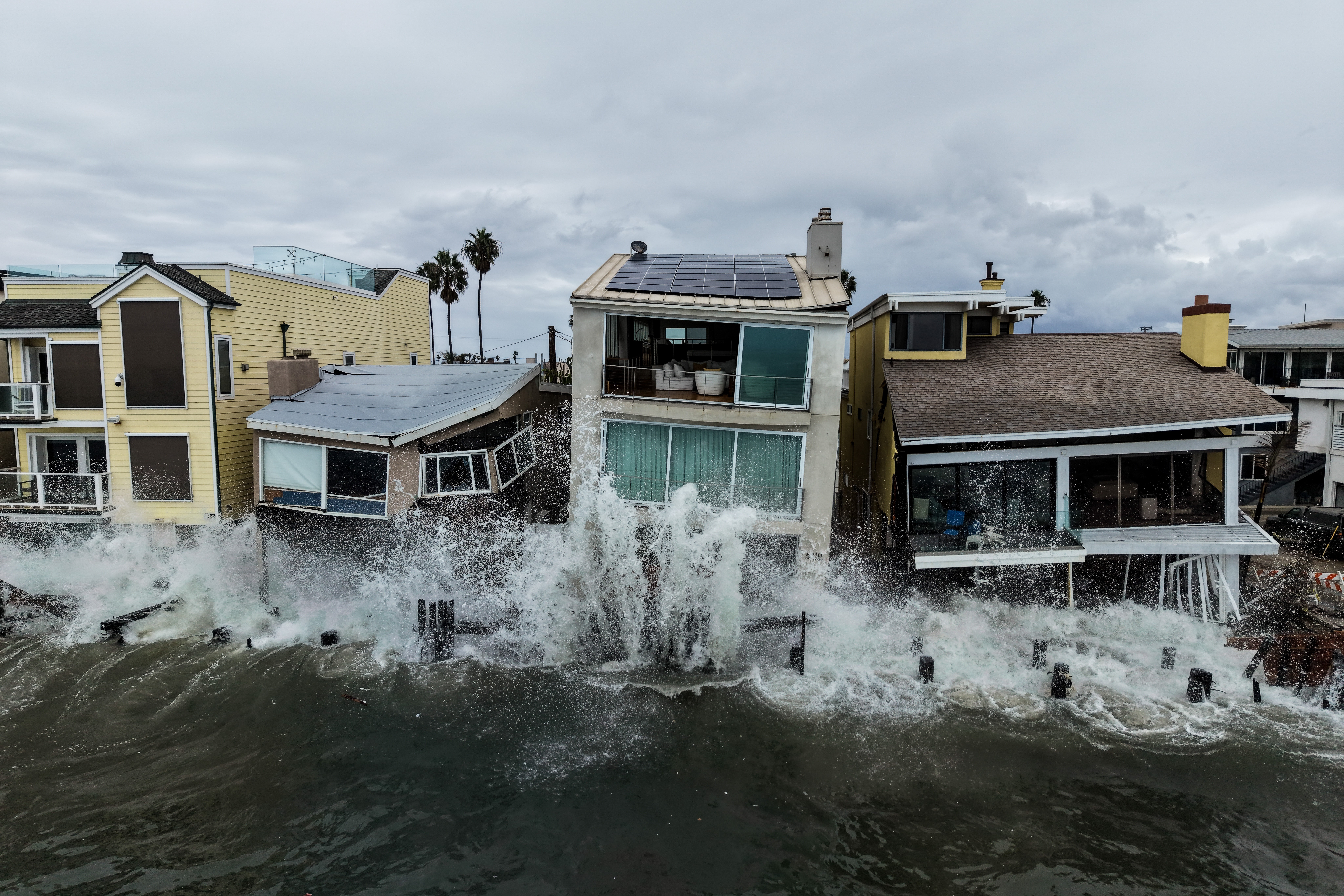 Storm waves crash into damaged beachfront homes.