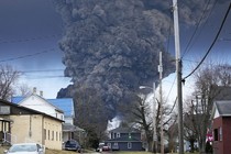 A huge black plume of smoke rises in the distance, captured from a residential neighborhood.
