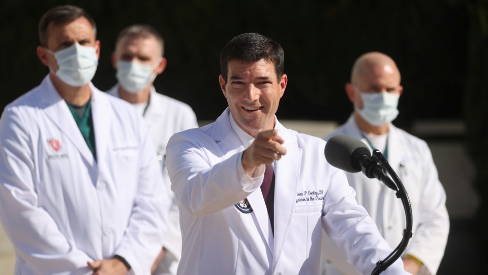 Trump's physician, Sean Conley, standing at a podium. He is smiling and pointing his finger.