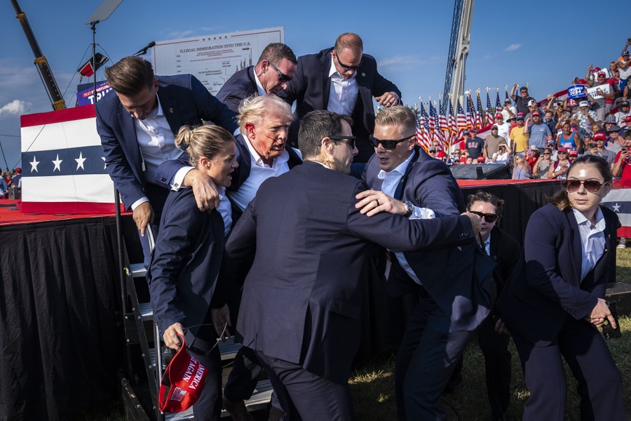 A group of Secret Service officers surround and escort Donald Trump, with a bloodied ear, off a stage at a rally.