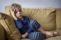 A boy looks bored sitting on a couch