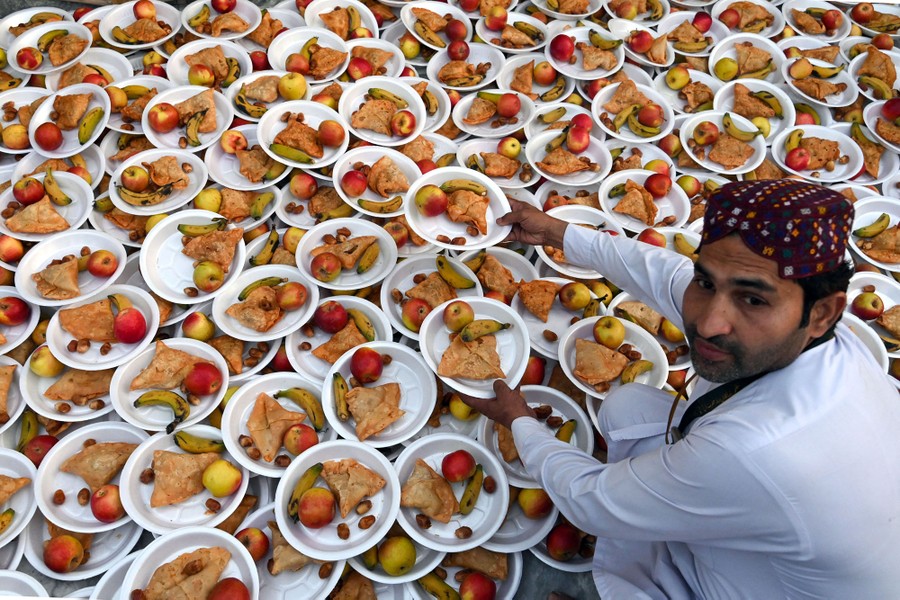 A person kneels down beside dozens of plates of food stacked on top of one another.
