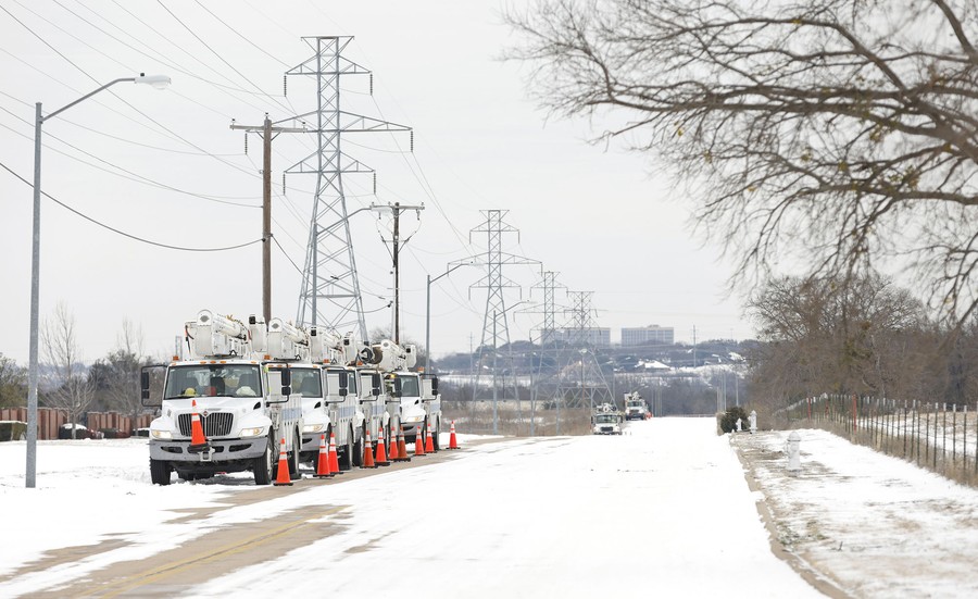 Service trucks park along a snowy road, near power lines.