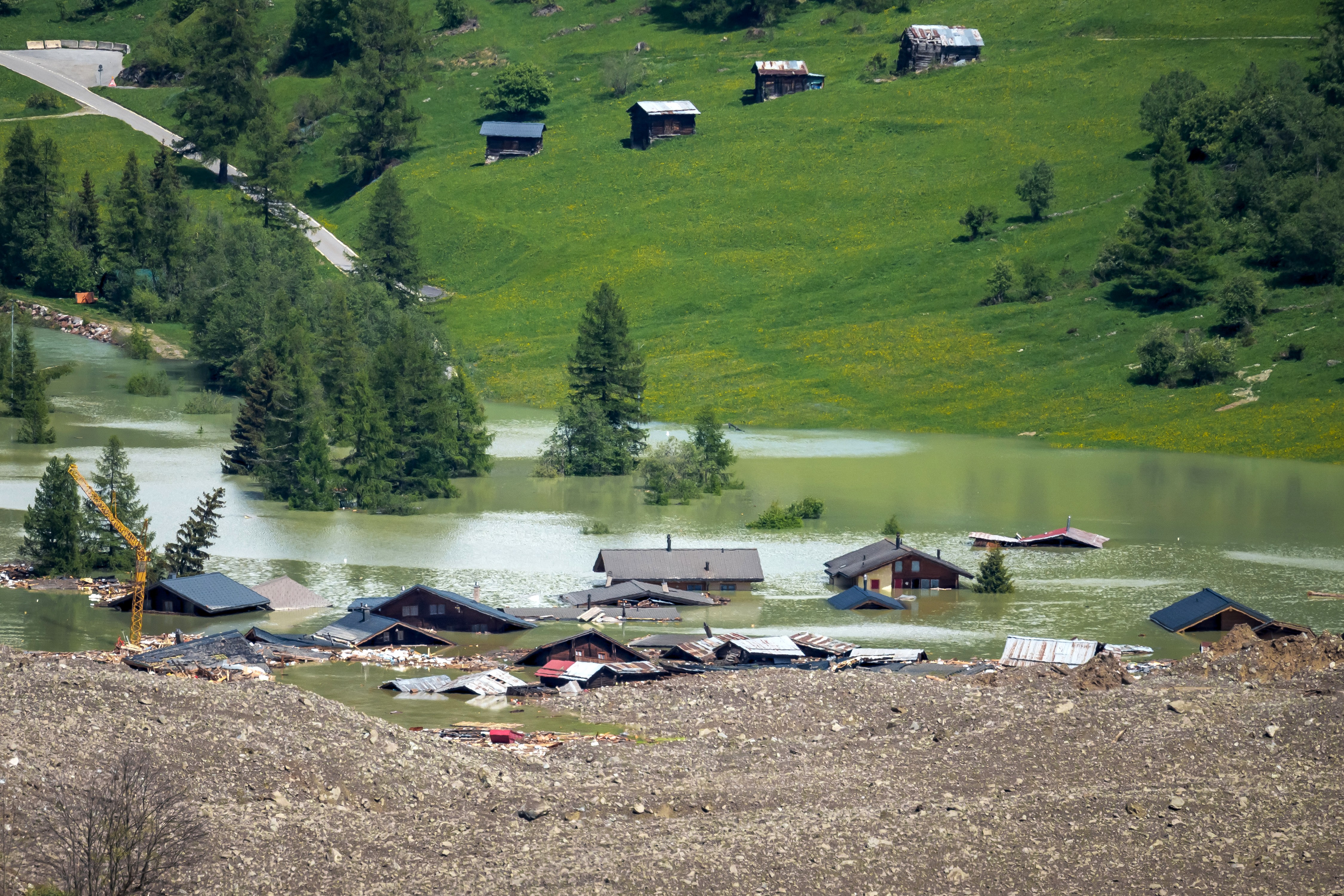 A cluster of houses sit in floodwater beside landslide debris.