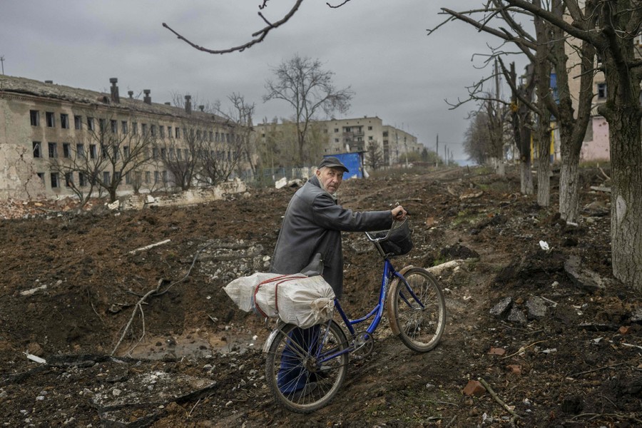 A man walks a bicycle on a heavily damaged road in Ukraine.