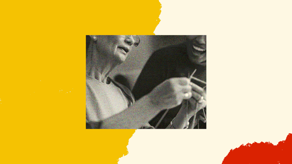 A black and white photo of two people knitting together.