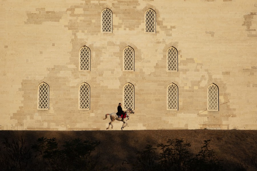 A man rides a horse in front of a wall of a historic building.