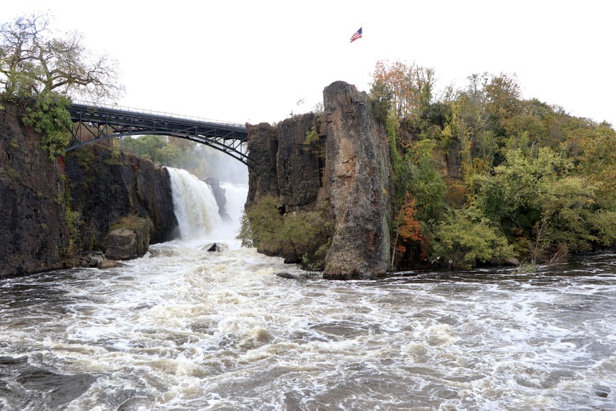 A view of a large waterfall seen beside a high bridge and stone cliffs.