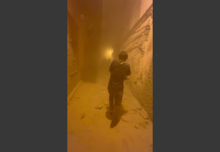 A person walks through a dust-filled alley.