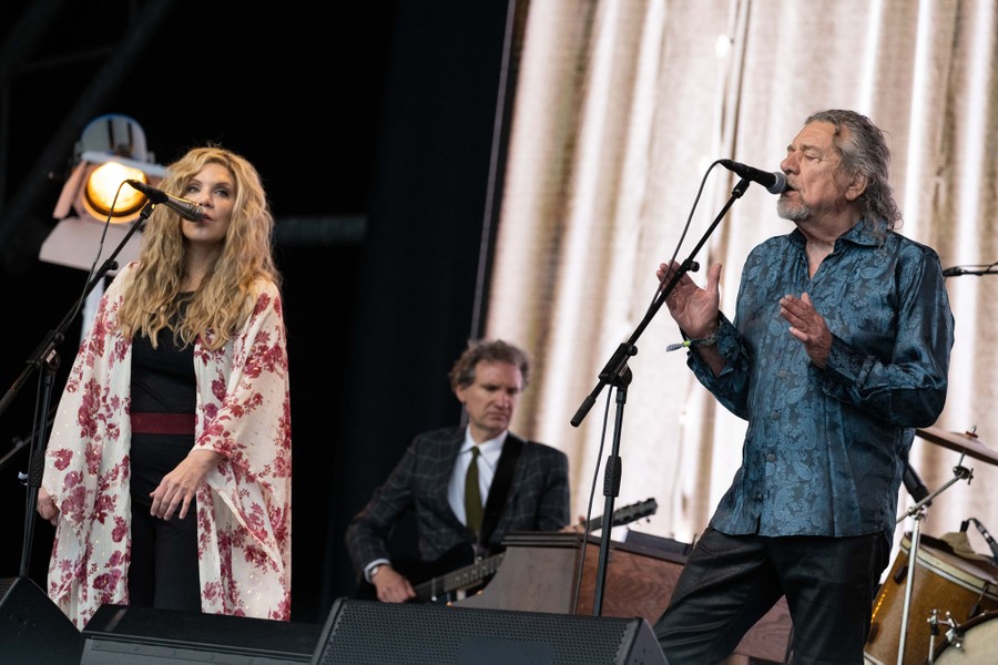 A woman and man sing into microphones on stage.