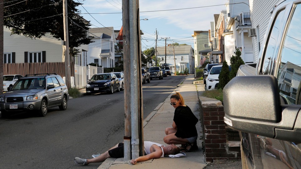 A woman crouches on the sidewalk next to her boyfriend, who is unresponsive and not breathing after an opioid overdose in the Boston suburb of Everett, Massachusetts, on August 23, 2017.