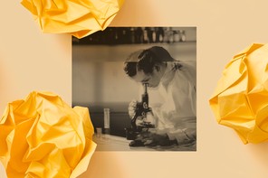 A blurry photo shows a light-skinned scientist in a white lab coat looking into a microscope.