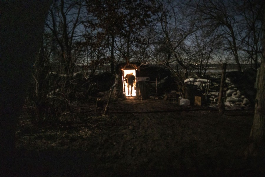 A soldier enters a well-lit bunker, as seen from outside, in a dark forest.