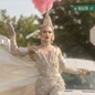 Sasha Velour, wearing a jumpsuit covered in crystals, walks down a street.