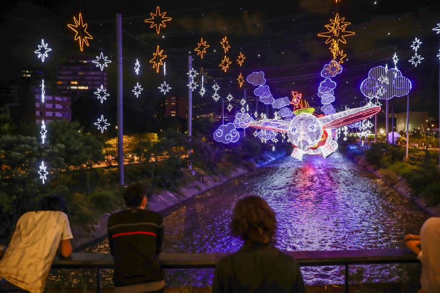 People look at decorative lights hanging over a narrow river channel.