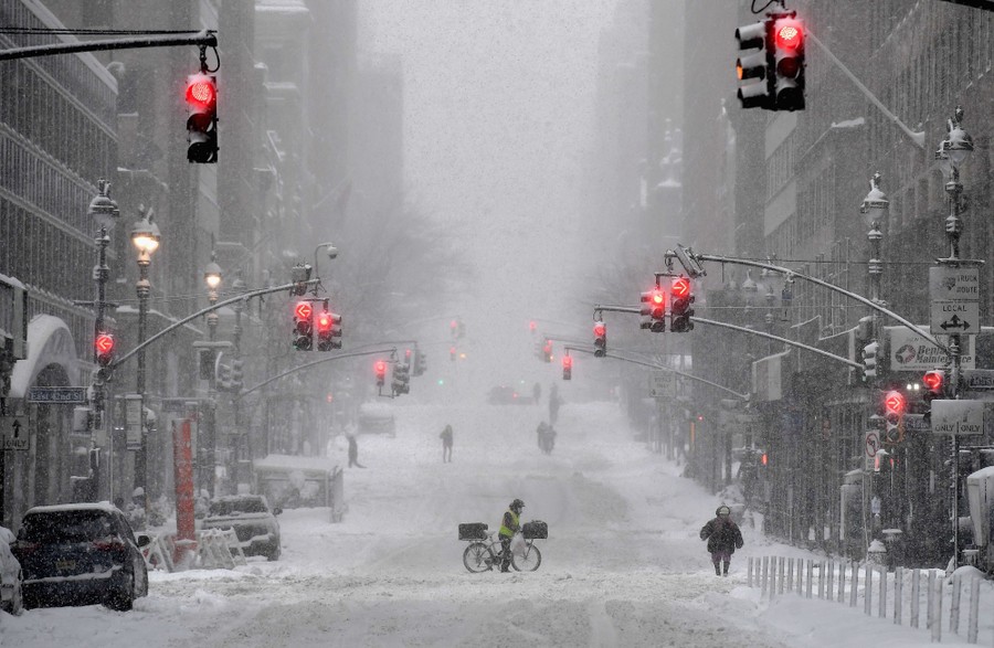 A few people walk in a deserted city street during a snowstorm.