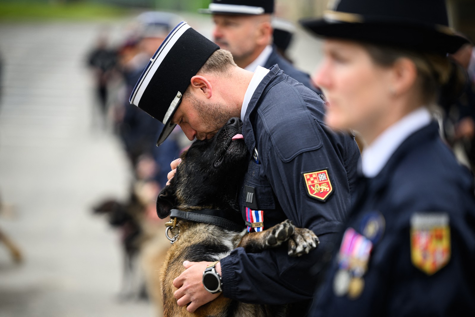 A police officer in dress uniform leans down to kiss his dog, as it stands on its hind legs, during a ceremony.