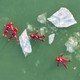 An aerial view of four people wearing bright-red rubber protective suits, floating in green-colored water among chunks of floating ice.