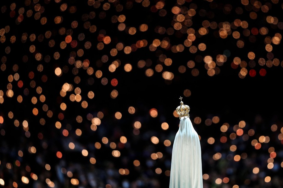 A small statue with dozens of blurred candles in the background