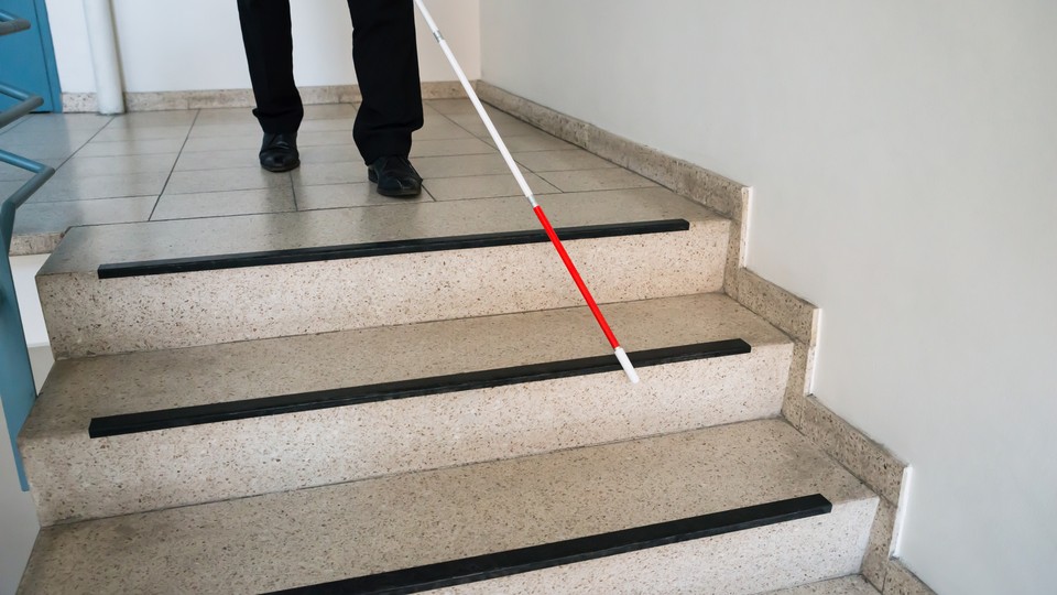 A man walks down a flight of stairs with the help of a white cane.