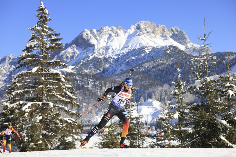 Skiers race through an alpine setting, with a tall snow-covered mountain in the background.
