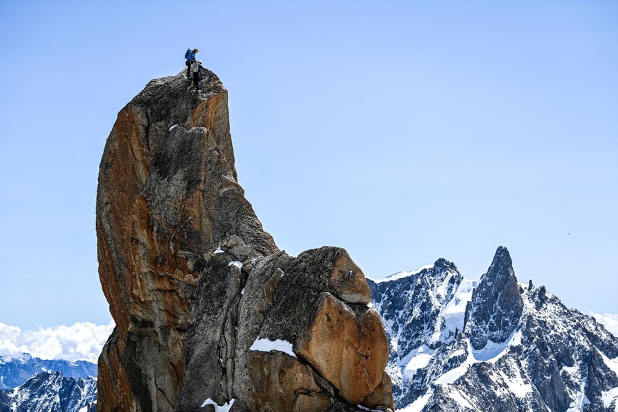 Mountain climbers scale a steep, bare, rocky mountaintop.