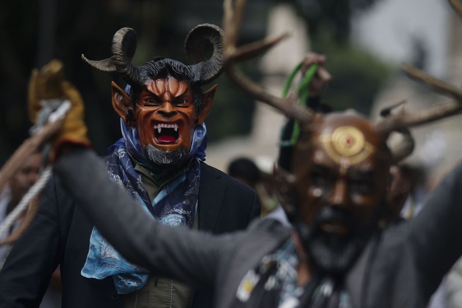 Performers wear frightening masks with horns in a parade.