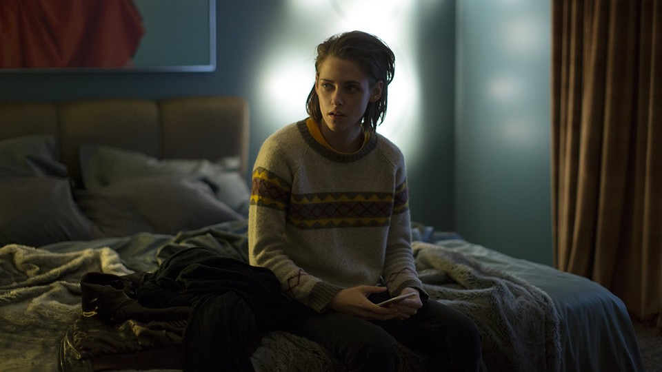 Kristen Stewart sitting on a bed with her phone in 'Personal Shopper'